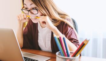 Lady in front of her computer, biting her pencil.